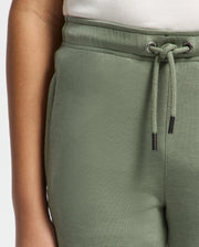 Close-up of a person wearing Psycho Bunny's KIDS DESERT EMBROIDERED SWEATPANT - B0P489F200 in soft stretch jersey with white drawstring, paired with a white shirt. Focus is on the waistband and pockets of these modal-blend pants against a plain white background.