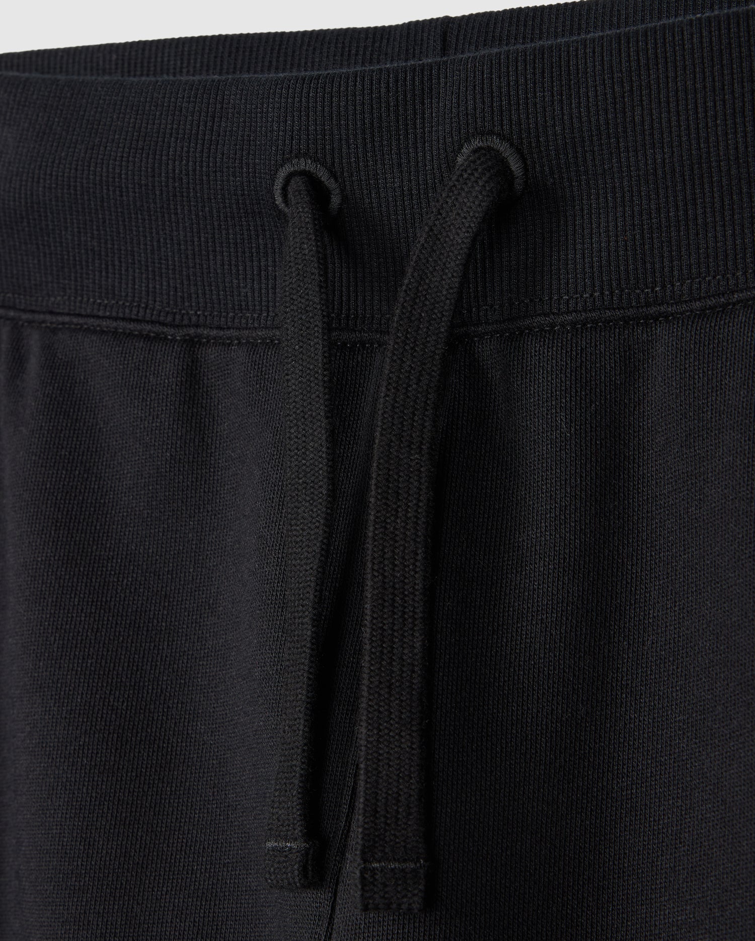 Close-up of the waistband of a pair of Psycho Bunny KIDS LEVY ESSENTIAL FLEECE SWEATPANTS (B0P721D200), showcasing the ribbed elastic band and black drawstrings hanging down the front. The fabric looks soft and smooth, making it perfect for cozy playtime.