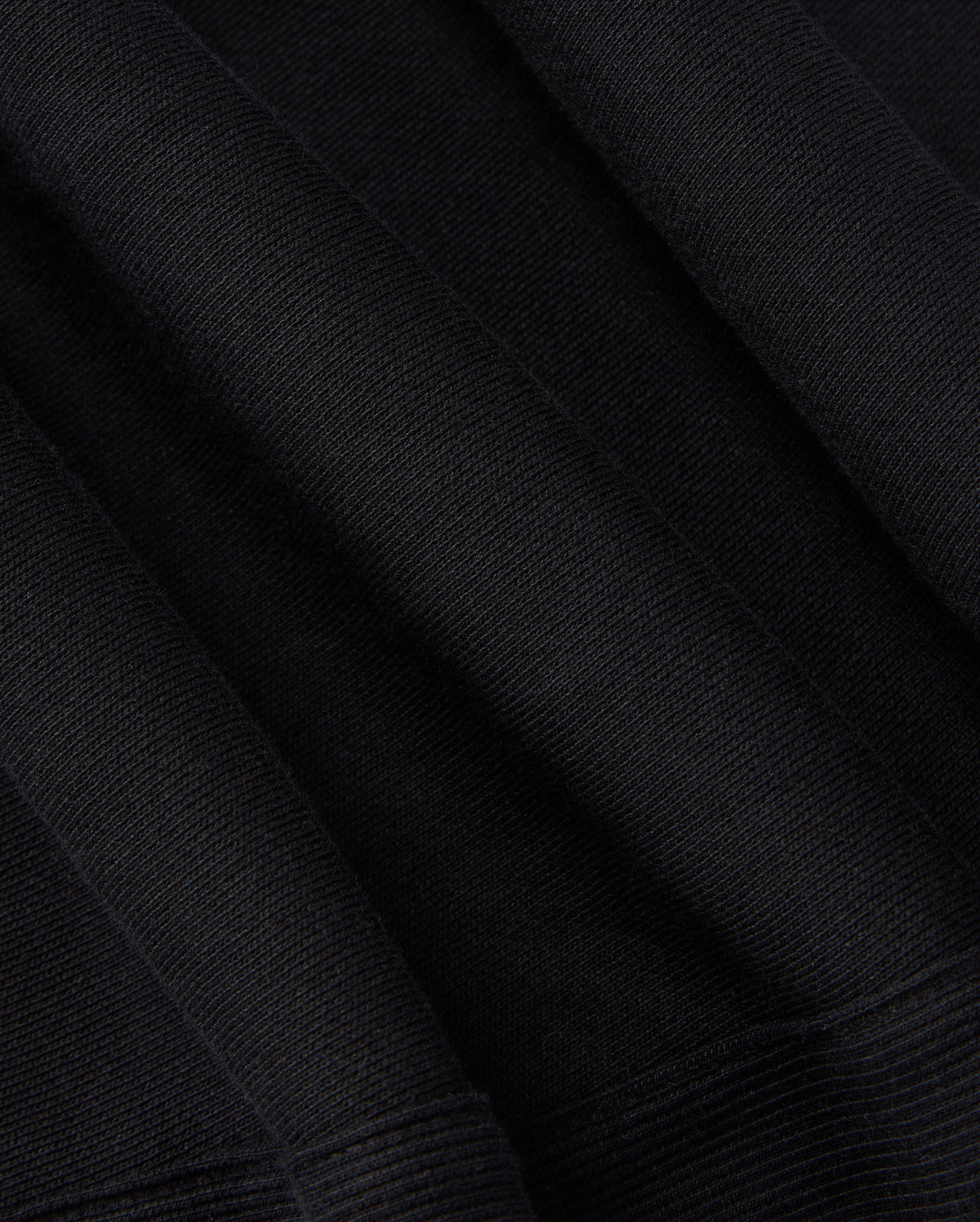 Close-up of the KIDS LEVY ESSENTIAL FLEECE SWEATPANT - B0P721D200 by Psycho Bunny. The black fabric has a ribbed texture and appears to have folds and creases, showcasing its thickness and material composition, much like cozy playtime pants. The texture suggests a soft and potentially warm fabric, ideal for clothing or upholstery needs.