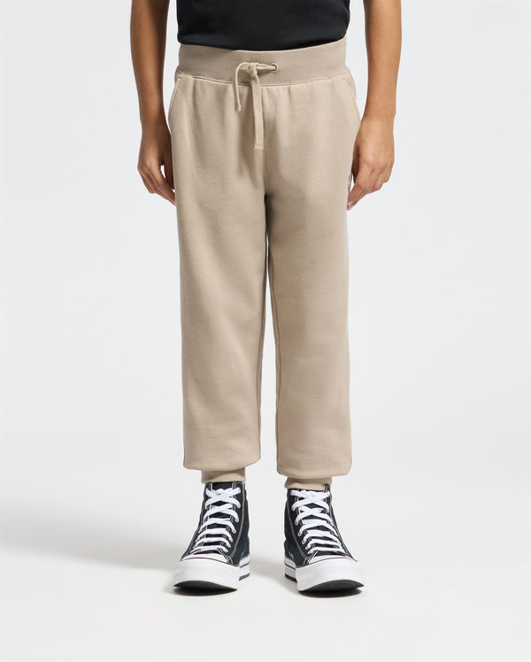 A person wearing a black shirt, the KIDS LEVY ESSENTIAL FLEECE SWEATPANT from Psycho Bunny featuring a cozy drawstring design, and black high-top sneakers stands against a plain white background, highlighting the comfort of their lower half.