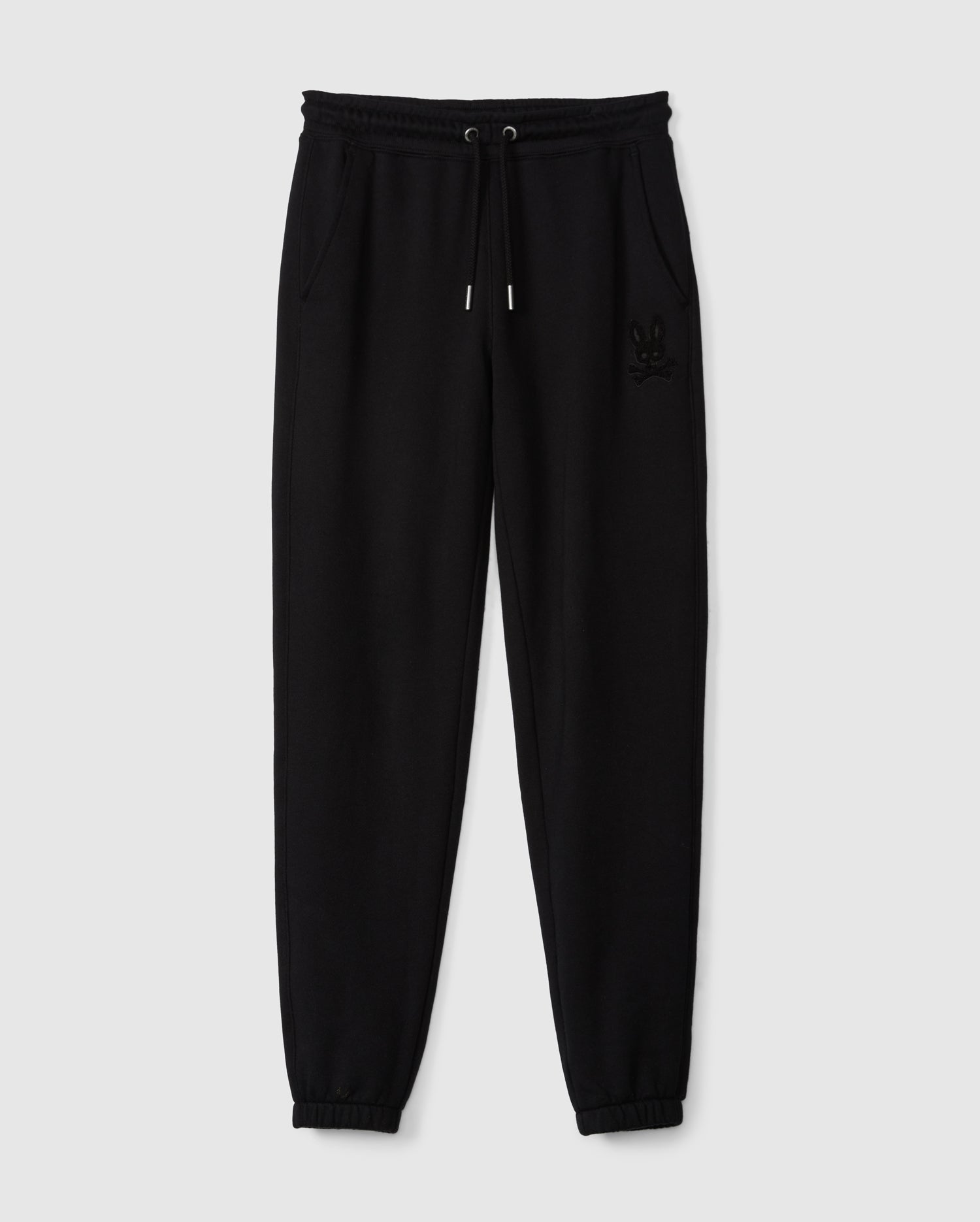 A pair of black Kids Pacific Chenille Jogger pants, designed by Psycho Bunny, featuring an elastic waistband with a drawstring and two side pockets. These joggers have elasticized ankle cuffs and are adorned with a subtle embroidered logo on the upper left side. Displayed against a plain light gray background, this setup perfectly highlights the casual style of these jogger pants.