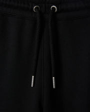 Close-up of black sweatpants, known as the KIDS PACIFIC CHENILLE JOGGER - B0P972D200 by Psycho Bunny, featuring a ribbed elastic waistband with a black drawstring. The drawstring has metallic tips, and the fabric appears soft and comfortable. A high-pile chenille logo patch adds a stylish touch to this casual bottom.