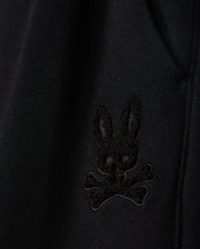 Close-up of the fabric from the KIDS PACIFIC CHENILLE JOGGER by Psycho Bunny, featuring an embroidered patch with a stylized black bunny head above crossed bones. This high-pile chenille logo patch adds a distinctive touch to any casual bottom or jogger pant.