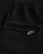 Close-up of a black fabric garment, possibly the Kids Pacific Chenille Jogger by Psycho Bunny, featuring a pocket with a horizontal zipper. The metallic zipper pull includes a small design or logo. The texture of the fabric appears soft and smooth, enhancing its casual bottom style.