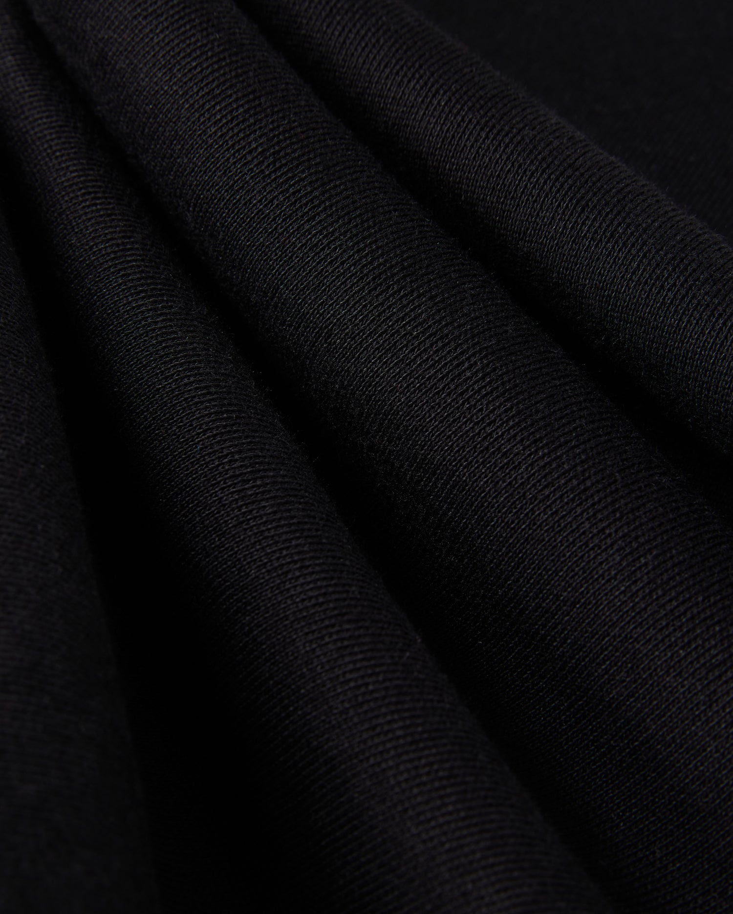 Close-up of folded black fabric with a smooth, textured surface, reminiscent of the KIDS PACIFIC CHENILLE JOGGER - B0P972D200 by Psycho Bunny. The material appears soft and evenly pleated, showcasing its fine fibers and subtle sheen under the light.