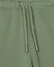 Close-up of the Kids Pacific Chenille Jogger from Psycho Bunny, showcasing green jogger pants with a drawstring featuring metal tips. These casual bottoms are made with textured fabric and visible stitching near the top edge, enhanced by a chenille logo patch for added style.