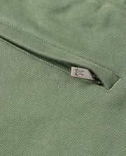 Close-up of the green **KIDS PACIFIC CHENILLE JOGGER - B0P972D200** by **Psycho Bunny**, featuring a subtle metal zipper detail. The zipper, adorned with a small decorative symbol on its pull tab, complements the jogger's textured woven pattern and casual bottom style.