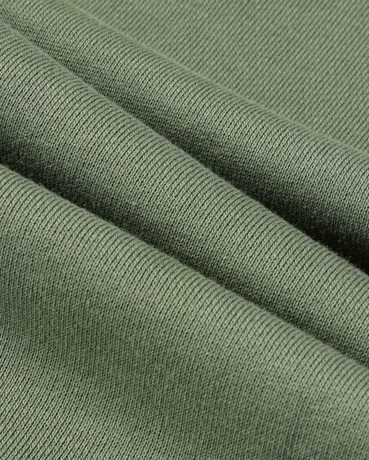 A close-up of a textured green fabric folded in layers, reminiscent of the KIDS PACIFIC CHENILLE JOGGER by Psycho Bunny. The ribbed pattern highlights its softness and thickness, with gentle diagonal folds creating shadows and highlights similar to those found in a jogger pant.