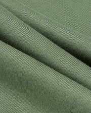 A close-up of a textured green fabric folded in layers, reminiscent of the KIDS PACIFIC CHENILLE JOGGER by Psycho Bunny. The ribbed pattern highlights its softness and thickness, with gentle diagonal folds creating shadows and highlights similar to those found in a jogger pant.