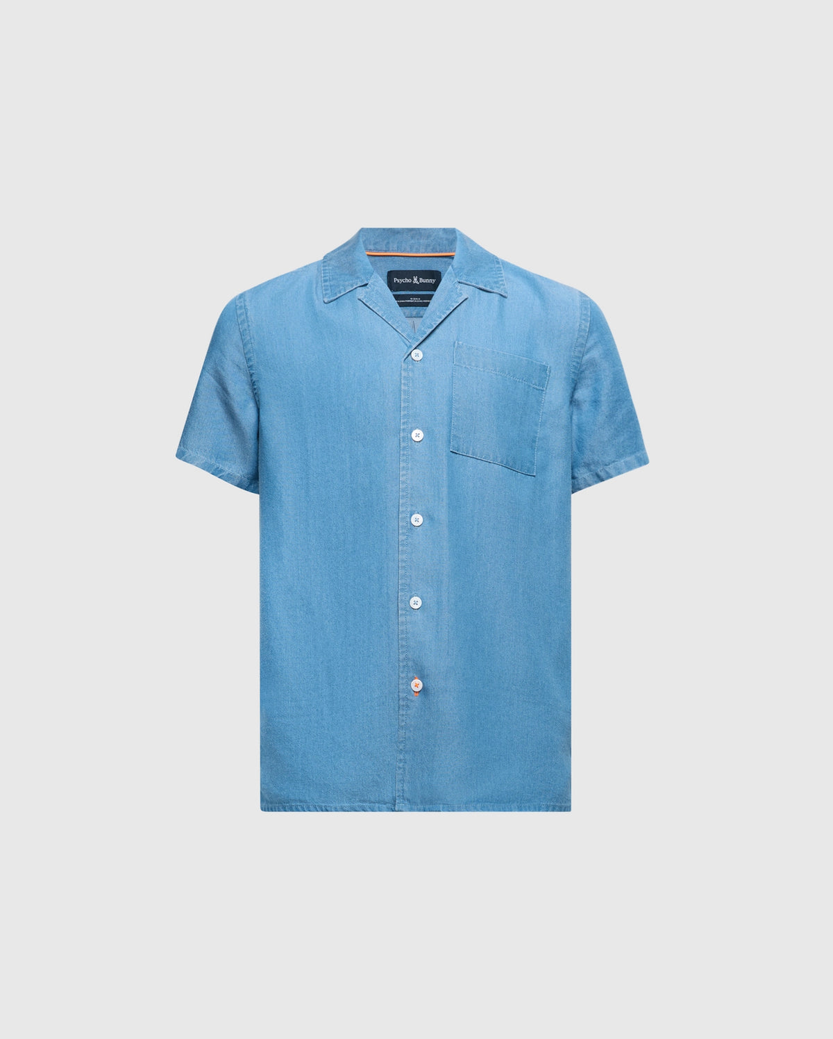 The KIDS KERVIN LIGHTWEIGHT DENIM WOVEN SHIRT by Psycho Bunny, in light blue with a front pocket and mother-of-pearl buttons, features a classic collar and casual style. Perfect for warm weather, it is displayed against a plain background. Product ID: B0Q467F200.
