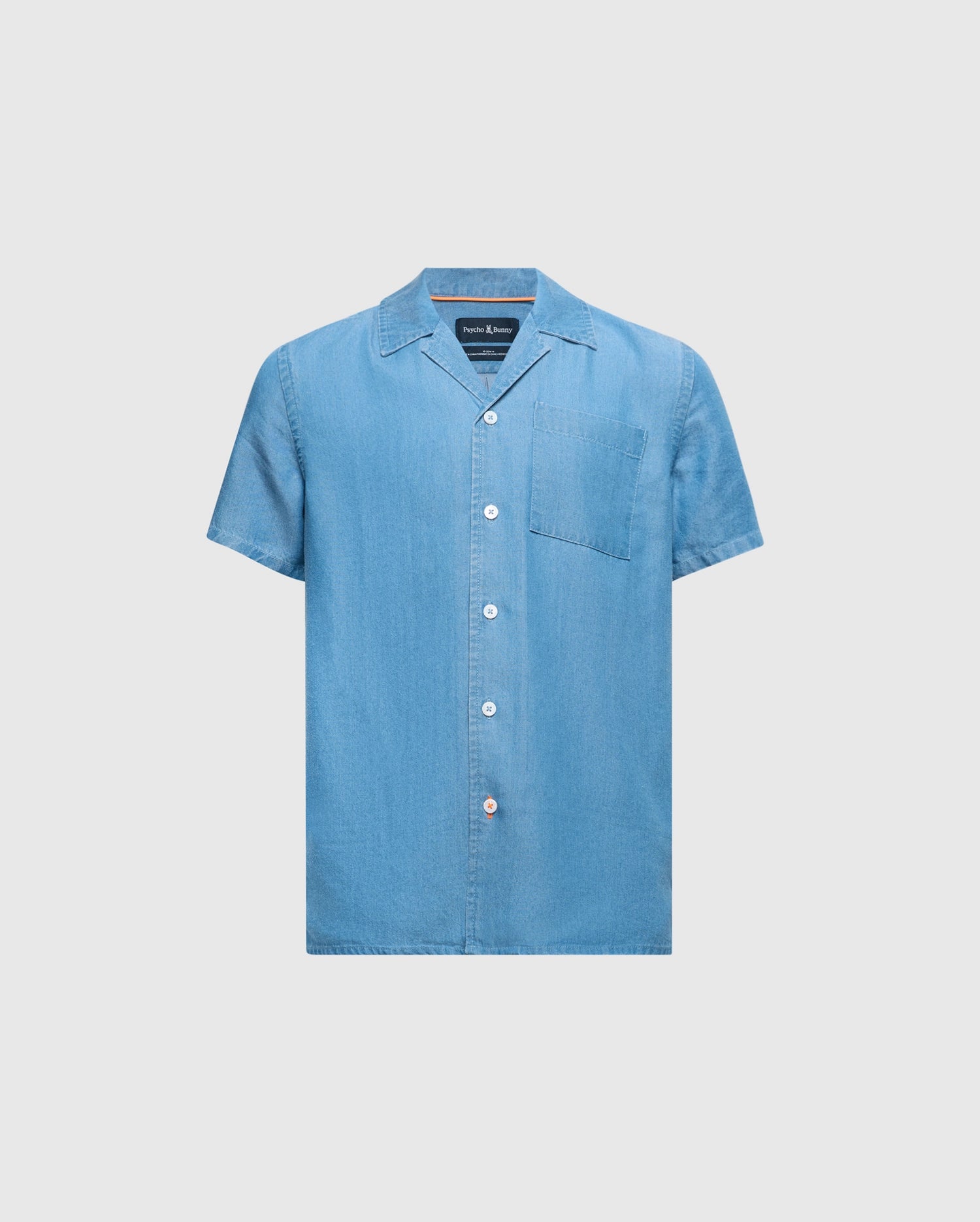 The KIDS KERVIN LIGHTWEIGHT DENIM WOVEN SHIRT by Psycho Bunny, in light blue with a front pocket and mother-of-pearl buttons, features a classic collar and casual style. Perfect for warm weather, it is displayed against a plain background. Product ID: B0Q467F200.