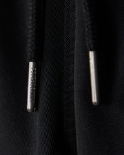 Close-up image of two black drawstrings with metallic tips, one labeled with the words "PSYCHO BUNNY". The background is a black fabric, possibly part of a hoodie or sweatpants featuring an embroidered Bunny logo. The clothing item in question is the KIDS WILLIS STRETCH TENCEL SHORT - B0R239Y1WB by Psycho Bunny.