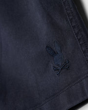 Close-up of navy blue Psycho Bunny kids' shorts crafted from KIDS WILLIS STRETCH TENCEL SHORT - B0R239Y1WB twill with an intricately embroidered logo featuring a rabbit. The texture of the material displays fine threading and detailing.