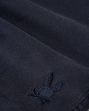 Close-up of Psycho Bunny kids' shorts made from dark KIDS WILLIS STRETCH TENCEL SHORT - B0R239Y1WB twill with a subtle, embroidered logo of a rabbit. The embroidery detail is in a slightly lighter shade of the same color as the fabric.