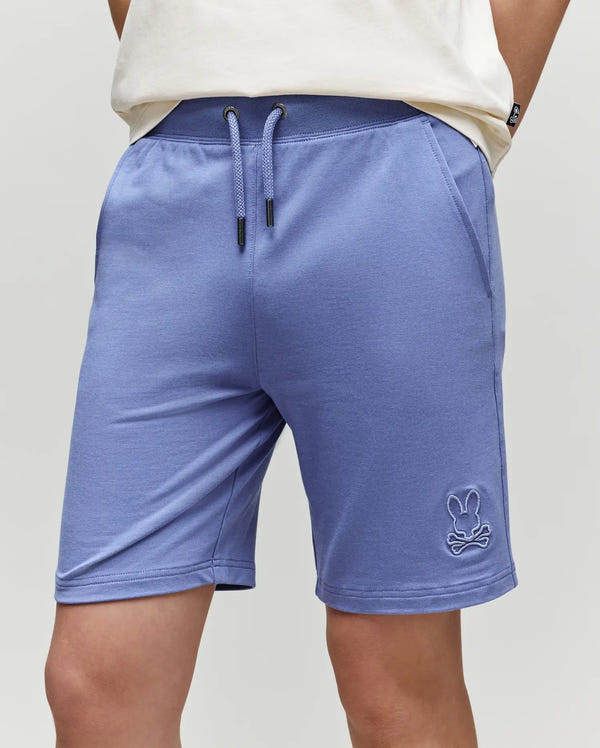 A person wears light purple Psycho Bunny KIDS LEVANZO FRENCH TERRY SWEATSHORTS (B0R578F200) made from micro French terry, with an embroidered Bunny logo on the left leg and a partially visible white shirt.