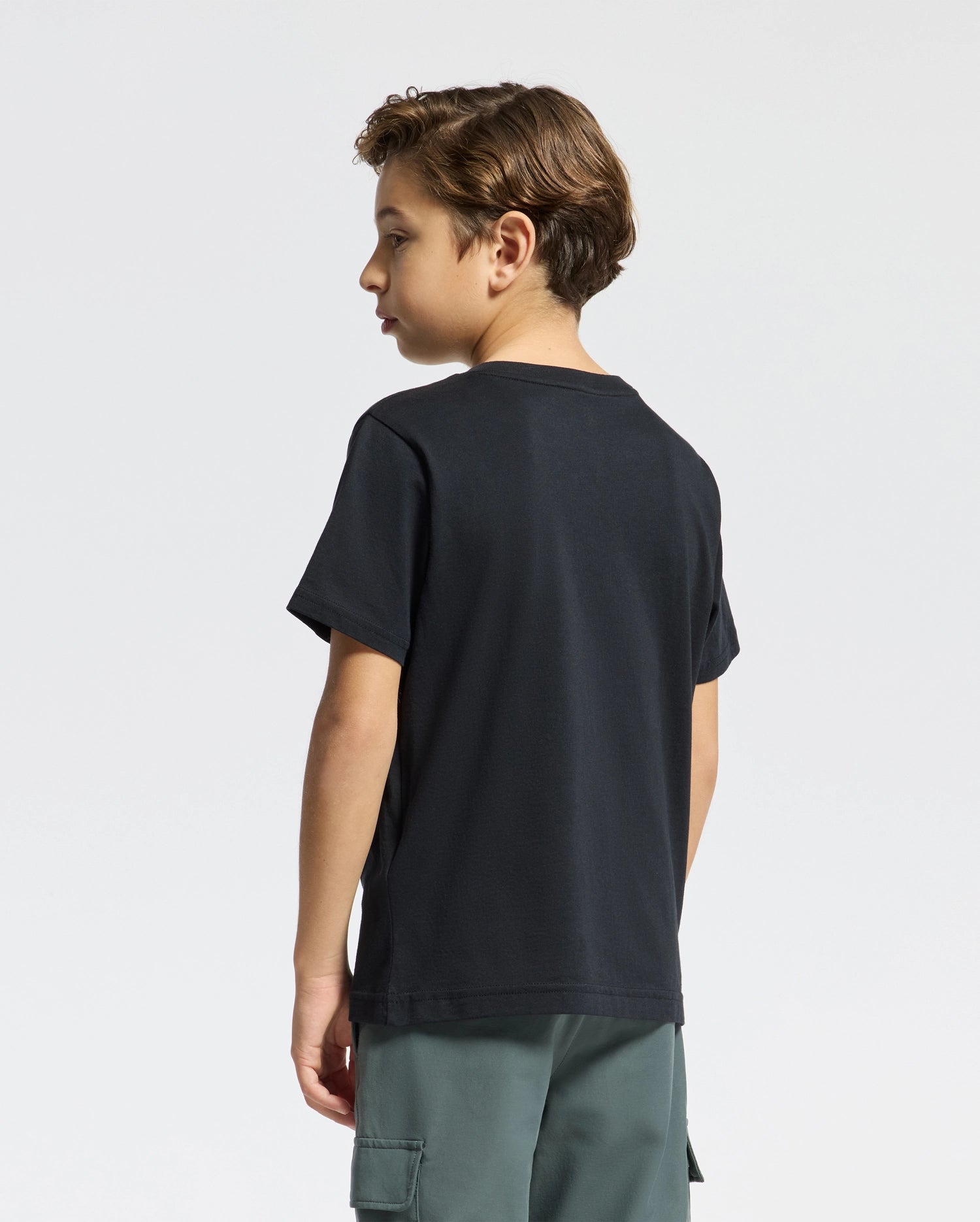 A young boy with short brown hair wears Psycho Bunny's KIDS CLASSIC CREW NECK TEE - B0U014CRPC, made of 100% Pima cotton, and green cargo shorts. Perfect for back-to-school outfits, he faces left against a plain white background.