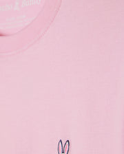 Close-up of the Kids Classic Crew Neck Tee (B0U014CRPC) by Psycho Bunny in pink, crafted from 100% Pima cotton. The fabric looks smooth and soft, and it features a small embroidered logo with bunny ears and facial details in black and white near the bottom edge—perfect for back-to-school outfits.