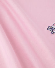 Close-up of pink fabric made from 100% Pima cotton, featuring a small embroidered design of a white skull and crossbones with bunny ears in the corner. This soft, smooth material with gentle folds is perfect for back-to-school outfits and ideal for Psycho Bunny's Kids Classic Crew Neck Tee - B0U014CRPC.