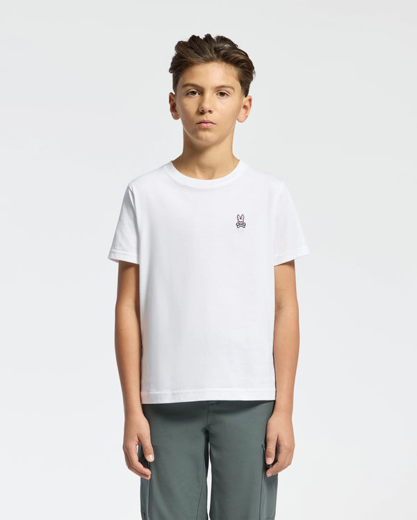 A young boy stands against a plain background, wearing Psycho Bunny's KIDS CLASSIC CREW NECK TEE - B0U014CRPC, made from 100% Pima cotton. The tee features a small bunny logo on the chest and is paired with gray pants. His neatly styled hair completes the back-to-school look.