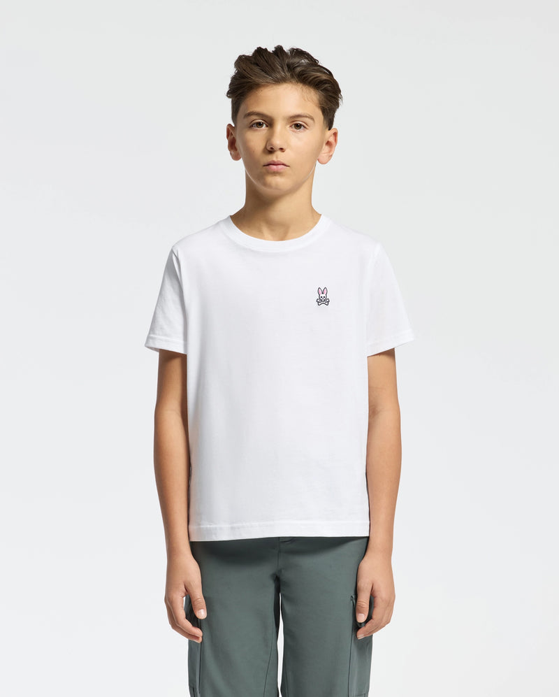 A young boy stands against a plain background, wearing Psycho Bunny's KIDS CLASSIC CREW NECK TEE - B0U014CRPC, made from 100% Pima cotton. The tee features a small bunny logo on the chest and is paired with gray pants. His neatly styled hair completes the back-to-school look.