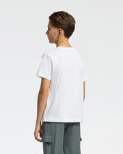 A boy with short brown hair stands sideways facing left, wearing the Psycho Bunny Kids Classic Crew Neck Tee (B0U014CRPC) in plain white and gray cargo pants against a white background—a perfect back-to-school outfit addition.