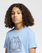 A person with curly hair is wearing a light blue KIDS MELBOURNE GRAPHIC TEE - B0U410F200 made from eco-friendly Peruvian Pima cotton. It showcases a bunny with crossbones and "Psycho Bunny" text on the front against a plain white backdrop.