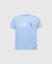The KIDS OCEANIA EMBROIDERED GRAPHIC TEE by Psycho Bunny, product B0U607F200, features retro light blue Pima cotton with embroidered bunny skull and crossbones in varying shades. Blue bunnies are on the right and a white bunny on the left. A small label decorates the bottom left hem.