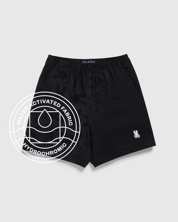 Psycho Bunny KIDS MALTA HYDROCHROMIC SWIM TRUNK (B0W321B2SW): Black trunks featuring a subtle water-activated bunny pattern and small white logo on the left leg. Circular overlay reads "Water Activated Fabric Hydrochromic" with droplet icon.