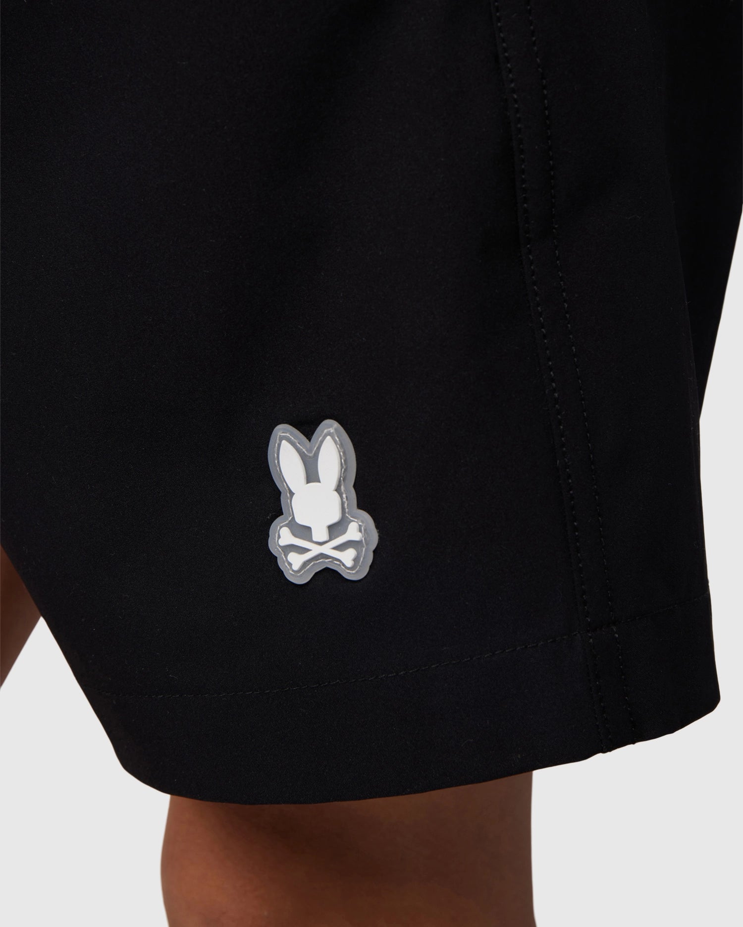 Close-up of a black polyester mechanical stretch fabric with a small, white Psycho Bunny logo on the lower right side, symbolizing the KIDS MALTA HYDROCHROMIC SWIM TRUNK - B0W321B2SW.