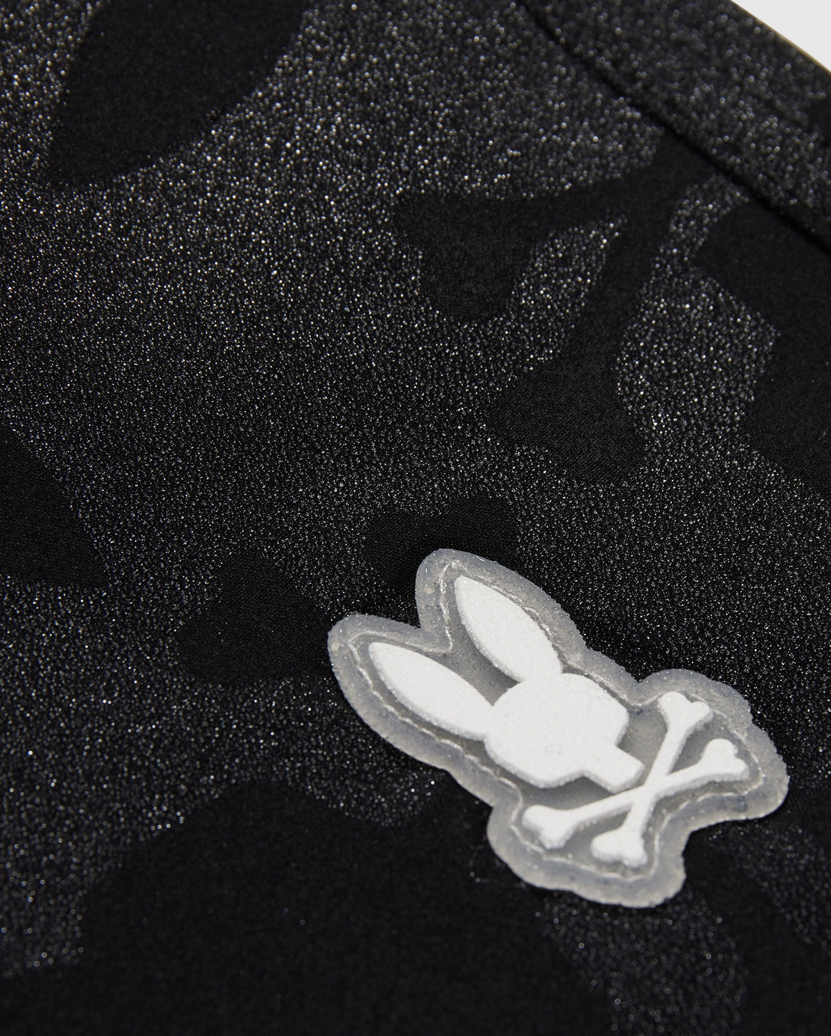 Close-up of a KIDS MALTA HYDROCHROMIC SWIM TRUNK - B0W321B2SW by Psycho Bunny, featuring a white embroidered logo of a stylized rabbit head.
