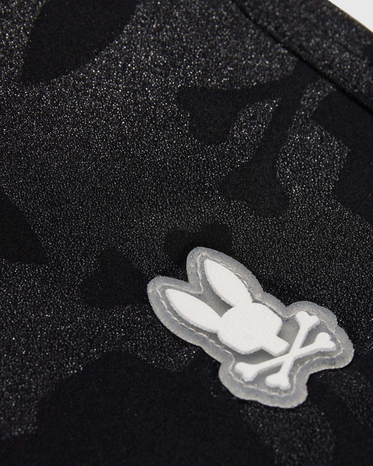 Close-up of a KIDS MALTA HYDROCHROMIC SWIM TRUNK - B0W321B2SW by Psycho Bunny, featuring a white embroidered logo of a stylized rabbit head.