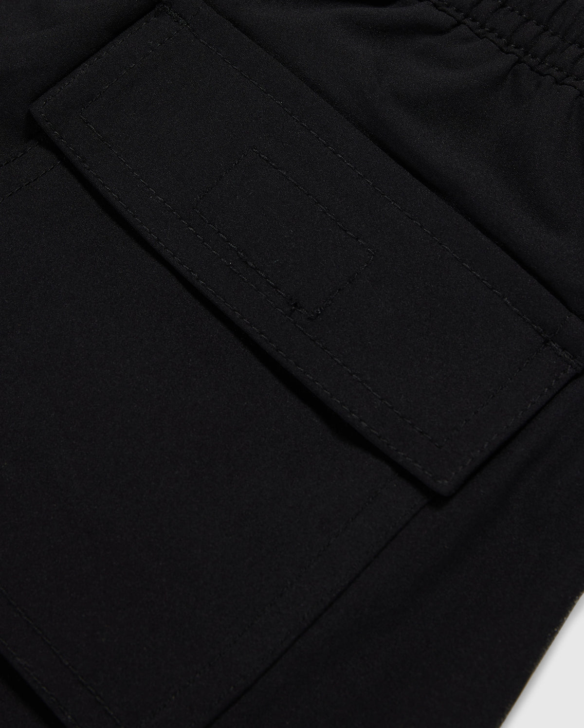 Close-up of a black polyester mechanical stretch fabric with a detailed view of a stitched rectangular patch pocket on Psycho Bunny's KIDS MALTA HYDROCHROMIC SWIM TRUNK - B0W321B2SW.