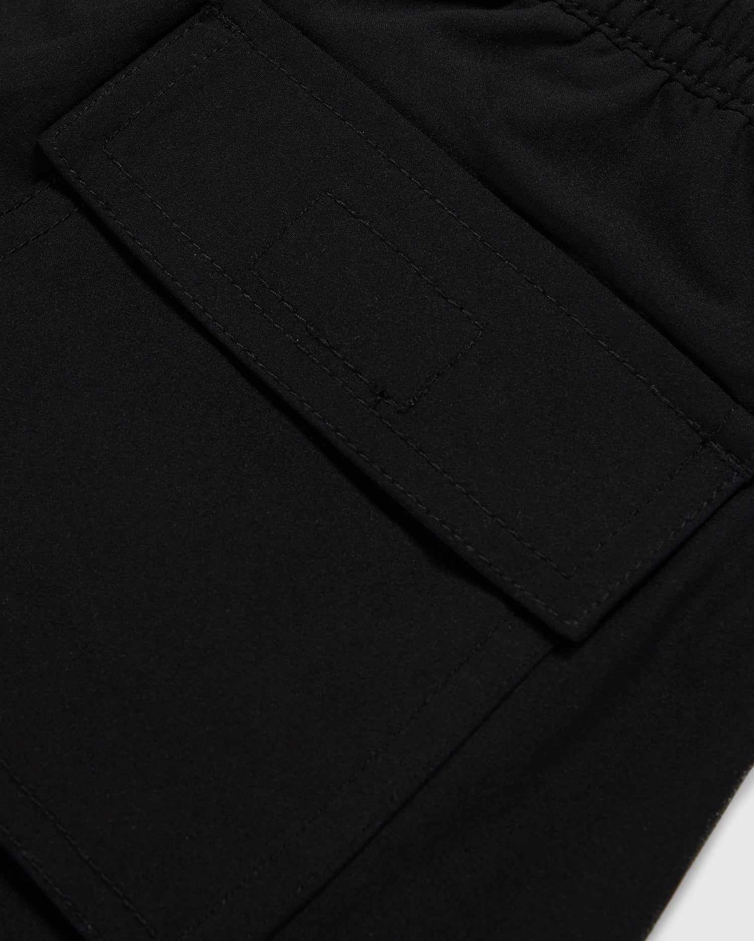 Close-up of a black polyester mechanical stretch fabric with a detailed view of a stitched rectangular patch pocket on Psycho Bunny's KIDS MALTA HYDROCHROMIC SWIM TRUNK - B0W321B2SW.