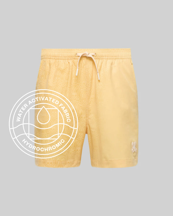 Psycho Bunny MENS SAMOS HYDROCHROMIC PRINTED SWIM TRUNK features light yellow fabric, mesh lining, subtle pattern, elastic waistband, drawstring, and small bunny logo. Water-activated hydrochromic technology with a droplet icon is highlighted on the left.