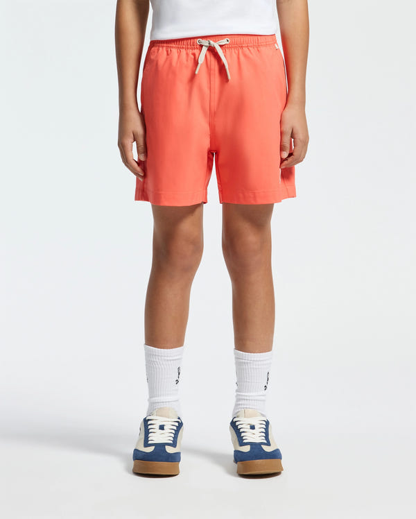 A person is wearing Psycho Bunny KIDS SAMOS HYDROCHROMIC SWIM TRUNK - B0W453F200, a white top, white socks, and blue-and-white sneakers with tan soles against a plain white background.