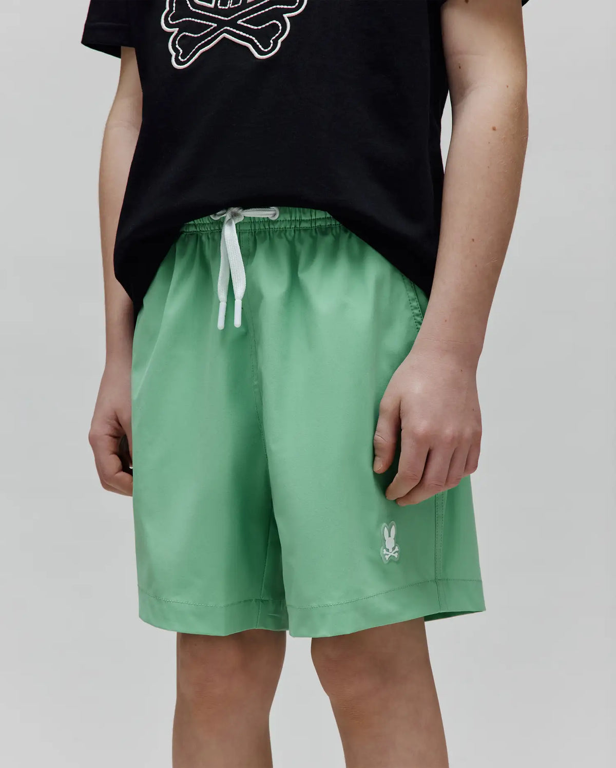 Kids Samos Hydrochromic Printed Swim Trunk in light green, featuring a relaxed fit, smooth fabric, white drawstring waist, and a small embroidered white Psycho Bunny skull logo on the left leg.