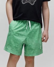 Kids Samos Hydrochromic Printed Swim Trunk in vibrant green, featuring an all-over tonal Psycho Bunny skull pattern, white drawstrings, and a small embroidered white logo on the right leg.