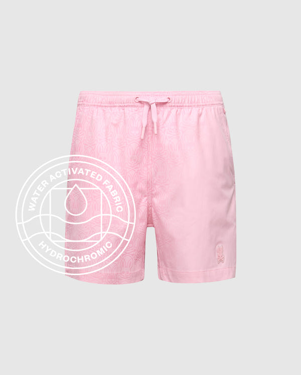 The Psycho Bunny KIDS SAMOS HYDROCHROMIC PRINTED SWIM TRUNK - B0W453F200 features a light pink color, subtle print, elastic drawstring waistband, and Hydrochromic technology. Overlay: "WATER ACTIVATED FABRIC HYDROCHROMIC" with droplet icon in circle.