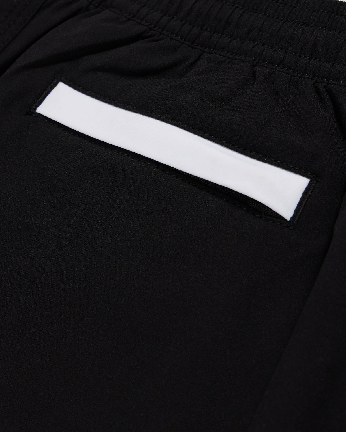 Close-up of Psycho Bunny KIDS PARKER HYDROCHROMIC SWIM TRUNK - B0W646C200 in black, showcasing a small pocket with a white strip above it. The fabric appears smooth and is quick-dry material. The pocket is integrated into the design, suggesting a sleek and minimalistic style.