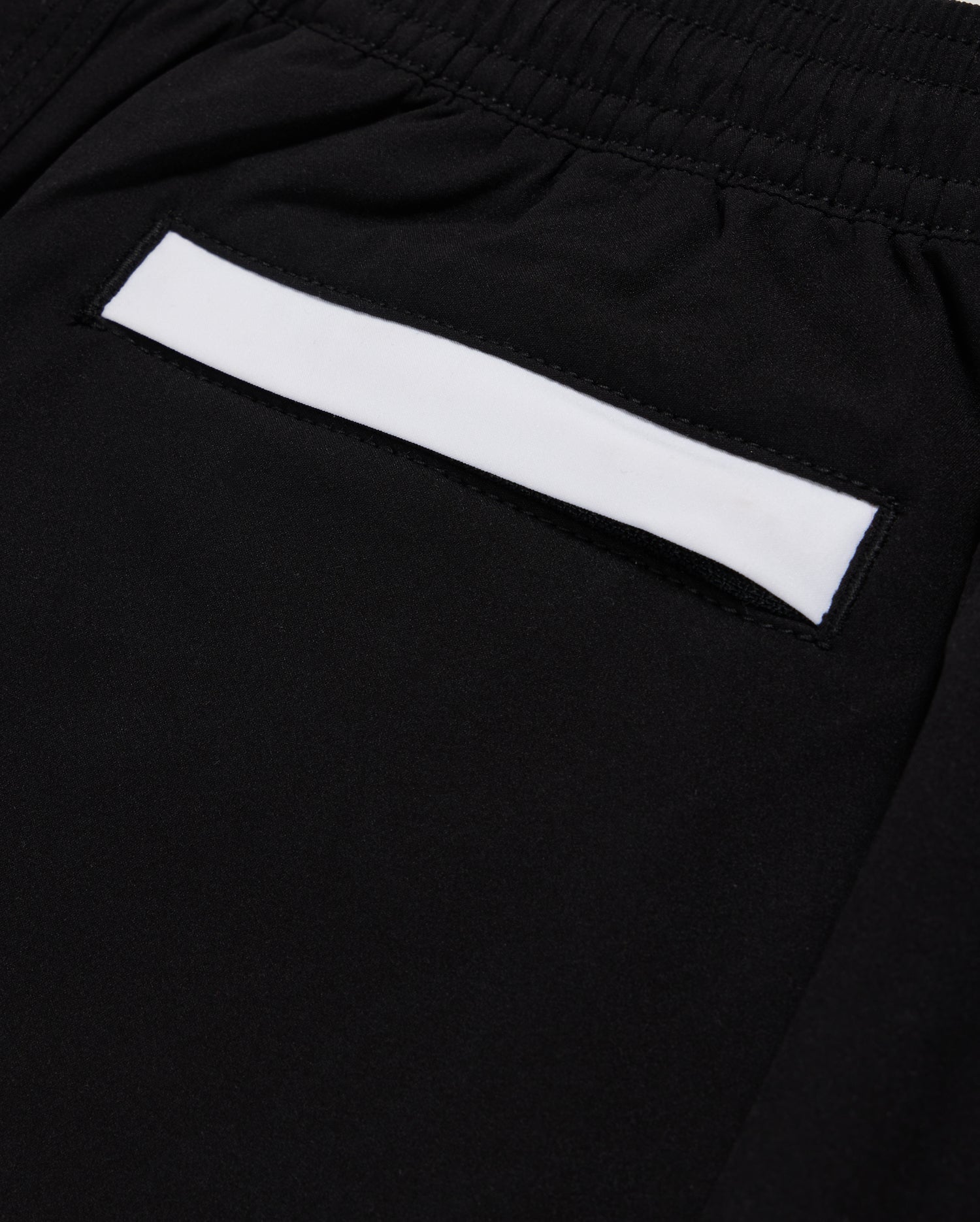 Close-up of Psycho Bunny KIDS PARKER HYDROCHROMIC SWIM TRUNK - B0W646C200 in black, showcasing a small pocket with a white strip above it. The fabric appears smooth and is quick-dry material. The pocket is integrated into the design, suggesting a sleek and minimalistic style.