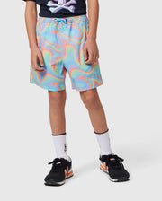 A person wearing colorful, swirly-patterned KIDS BLOOMINGTON SWIM TRUNK - B0W941A2PO by Psycho Bunny with blue, orange, and yellow hues stands against a plain background. They also wear black and red sneakers with white socks. The person’s upper body is mostly out of the frame, showing only part of a black shirt with a graphic.