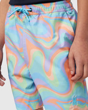 A person wearing colorful, wavy-patterned Psycho Bunny KIDS BLOOMINGTON SWIM TRUNK - B0W941A2PO with a blend of pastel green, blue, orange, and purple. The quick-drying shorts feature a blue drawstring and a small silicone Bunny patch on the left leg. Only the torso and part of the thighs are visible.