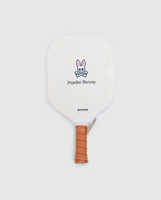 The PICKLEBALL PADDLE WITH COVER - B6A277E200 by Psycho Bunny features a white face, tan leather grip, and an embroidered pink and black bunny logo above "Psycho Bunny," plus a polypropylene honeycomb core.