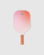The Psycho Bunny PICKLEBALL PADDLE WITH COVER - B6A277E200 features a gradient pink-orange face, tan perforated grip, cartoon bunny with crossbones at the top center, and a durable honeycomb core for enhanced performance.