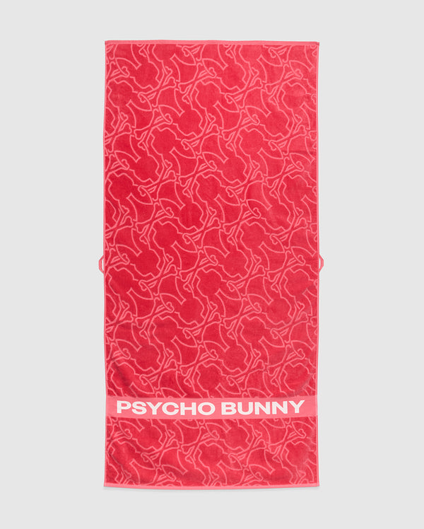 A red Psycho Bunny towel, model B6A287F200, is crafted from plush terrycloth cotton. It features abstract bunny designs and a solid red band at the bottom edge with the iconic white "PSYCHO BUNNY" text, merging style and comfort in premium apparel.