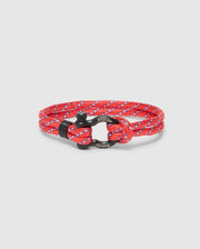 The Psycho Bunny Men's Rope Bracelet (B6A368E200) features a braided red and blue nylon rope with a black metal clasp engraved with "Psycho Bunny," adding sophistication. The elegant bracelet is neatly coiled on a light gray background.
