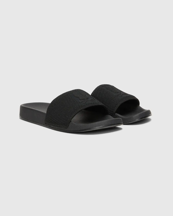 The MENS KNIT SLIDES - B6A474F200 by Psycho Bunny are black slide sandals with textured knit textile straps on a plain gray background. They feature an open-toe design, a molded footbed for comfort, and a flat, thick sole.