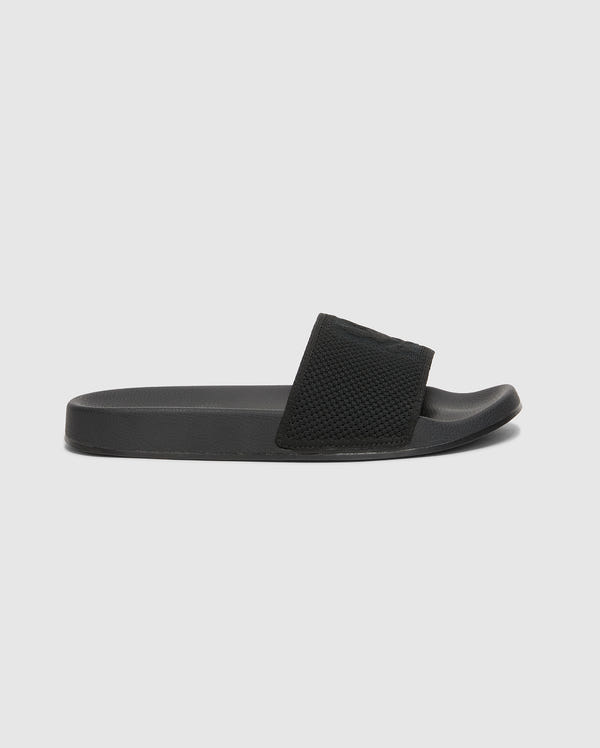 The Psycho Bunny MENS KNIT SLIDES - B6A474F200 are black slide sandals with textured straps, flat soles, and molded footbeds for comfort. Displayed against a white background, they feature an open toe design.