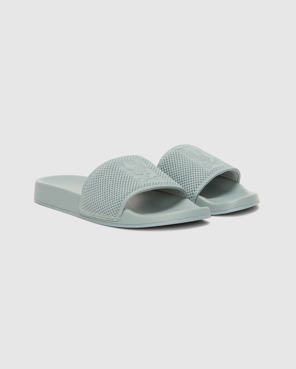 The Psycho Bunny MENS KNIT SLIDES - B6A474F200 are light green sandals with textured wide straps and an ergonomically molded footbed for comfort, shown on a plain white background.