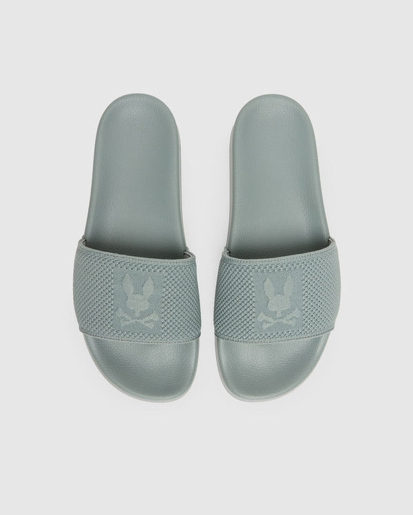 A pair of Psycho Bunny MENS KNIT SLIDES (B6A474F200) in sage green knit textile with textured, eagle-embossed straps and an ergonomically molded footbed, shown from above on a plain white background.